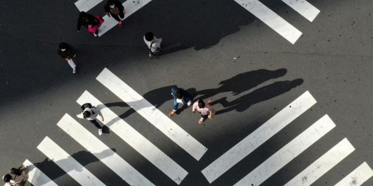 People cross a street in front of Shinjuku station, a normally crowded street during the weekend.