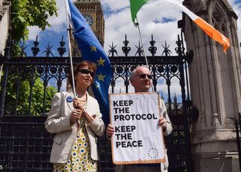 Protestors outside UK Parliament with a placard reading, "Keep the protocol, keep the peace."