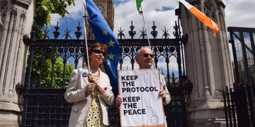 Protestors outside UK Parliament with a placard reading, "Keep the protocol, keep the peace."